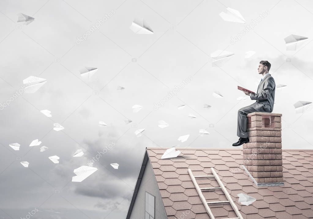 Young businessman sitting on house roof 