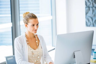Masada oturan ve bilgisayarda çalışarak çekici genç kadın