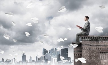Elinde kırmızı kitap ile üst yapı üzerinde oturan genç işadamı