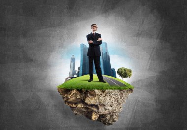 Yeşil yüzen adada beton zemine karşı duran kendine güvenen zarif iş adamı.