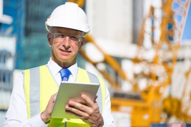 Kıdemli mühendis erkek takım elbise ve tablet PC'de inşaat sitesinde güneşli gün çalışan kask
