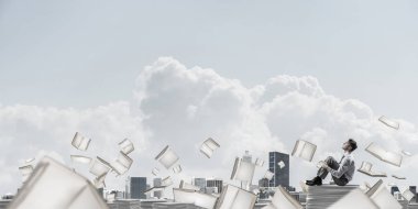 İş adamı uzak belgeler arasında kitap Clear sky ile arka plan üzerinde uçan yığını üzerinde otururken arıyorum. Karışık teknik.