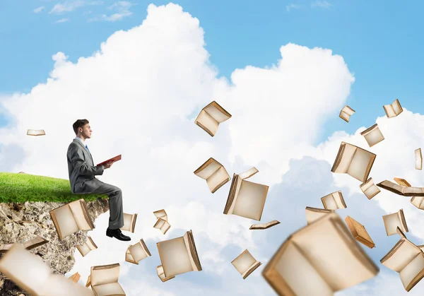 Genç işadamı ellerinde kırmızı kitap uçurumun kenarında yüzen