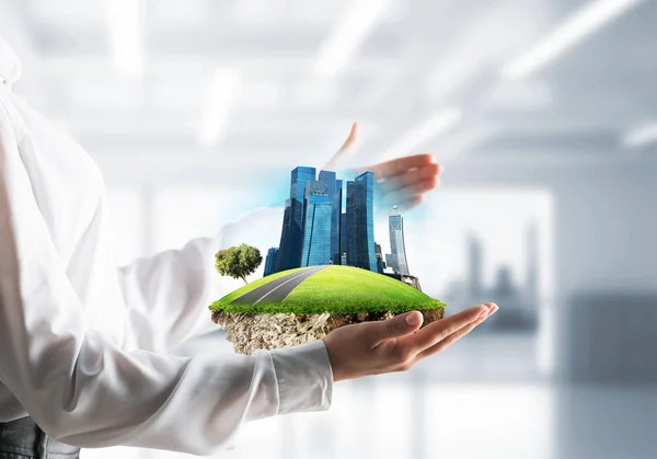 Closeup of business woman in shirt keeping green island with skycraper city in her hands with office view on background.