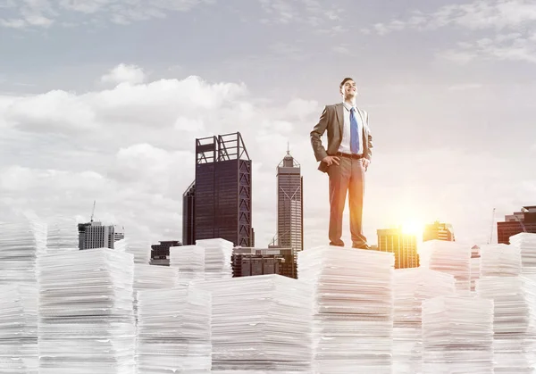 Homme d'affaires en costume debout sur une pile de documents — Photo