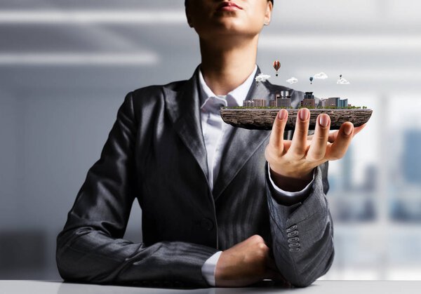 Обрезанный образ бизнесмена в костюме, представляющий в руке современный городской квартал с видом на офис на заднем плане
. 
