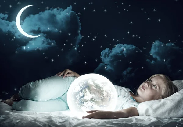 月の惑星が付いているベッドに座っているかわいい女の子 — ストック写真