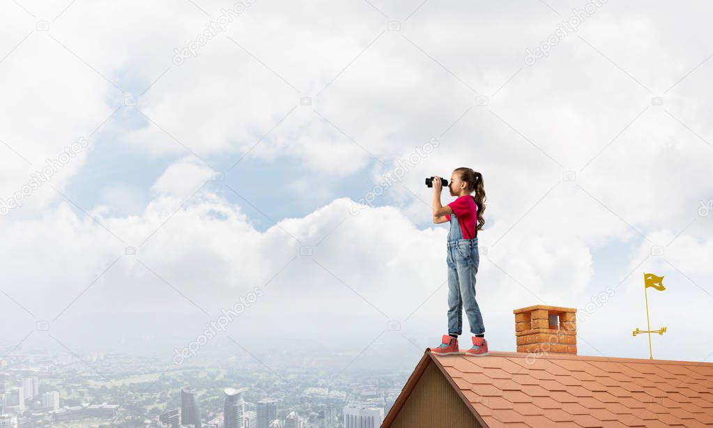 Cute girl of school age on building roof looking in binoculars