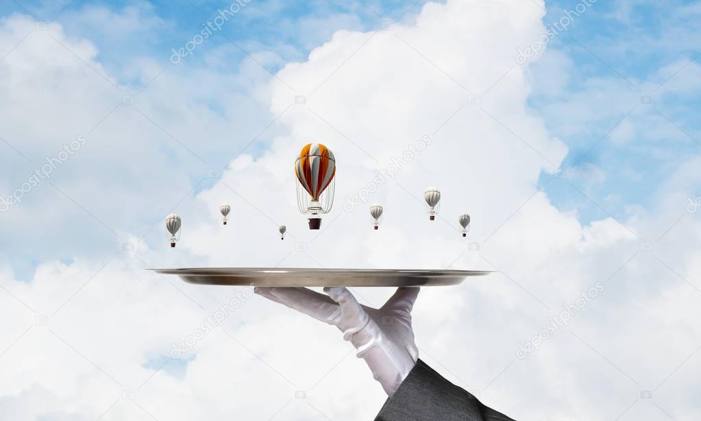 Closeup of waiter hand in glove presenting flying aerostats on metal tray with blue cloudy skyscape on background, 3D rendering