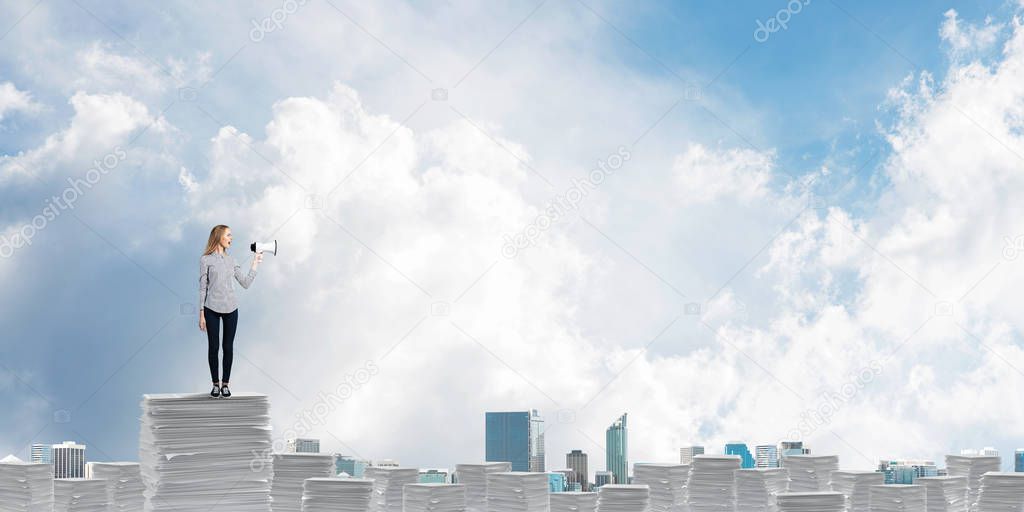 Woman in casual clothing standing on pile of documents with speaker in hand with skyscape and city view on background. Mixed media.