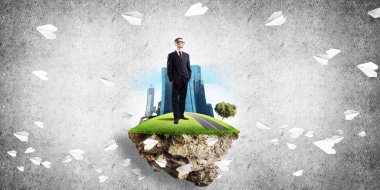 Yeşil yüzen adada beton zemine karşı duran kendine güvenen zarif iş adamı.