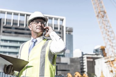 Kıdemli mühendis kostümlü ve kasklı konuşan cep telefonu.