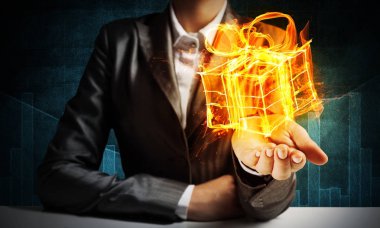 İşadamı elinde yanan hediye kutusu ile koyu arka plan sunulması takım elbiseli Resim kırpılmış.