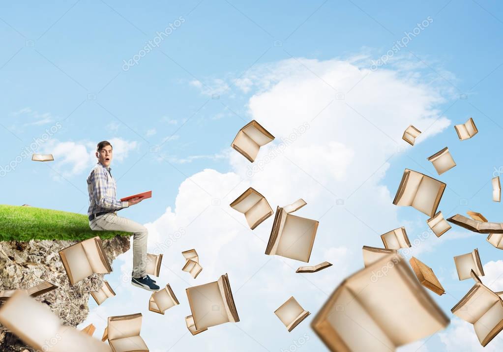Young man floating on island in blue sky with red book in hands