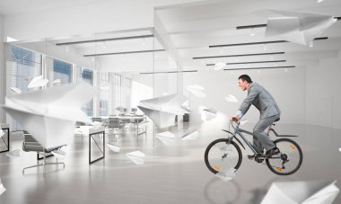 Elinde kağıt belgeler olan işadamı. İş elbisesi içinde muhasebeci uçan kağıt uçaklar ile konferans odasında bisiklet sürme. Modern iş alanı ile kurumsal ofis hayatı konsepti