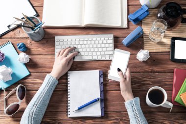 Ofis masasında akıllı telefon kullanan bir iş kadını. Çevrimiçi iş uygulaması kavramı. Kadın eli ve klavyesi olan düz bir ofis işyeri. İş için dijital teknoloji ve mobil uygulama.