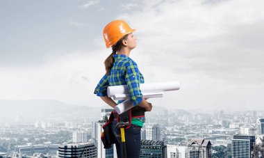 Teknik planlarla donatılmış kadın mühendis var. Kareli mavi gömlekli kadın mimarın şehrin arka planındaki inşaatı teftiş edişinin yan görüntüsü. Proje yönetimi inşa ediliyor