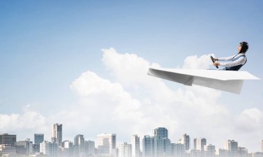 Havacı şapkalı işadamı kağıt düzlemde oturuyor ve direksiyonu tutuyor. Pilot yüksek gökdelenler ve ofis binaları ile iş merkezi üzerinde kağıt uçak sürüş. Bulutlu mavi gökyüzü arka plan