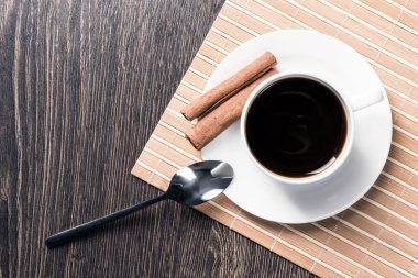 Tahta masada bir fincan espresso kahvesi. Üst manzara beyaz porselen bardak ve çay tabağına tarçın çubukları. Kafedeki taze ve aromatik sıcak içeceği kapat. Sabah kahvesi ve mola zamanı konsepti.