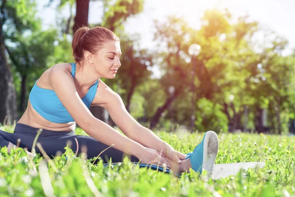 公園でヨガをやってスポーツウェアの魅力的な女の子 緑の芝生の上でヨガポーズに座っている若い女性 晴れた夏の日にスポーツトレーニング屋外 朝ストレッチ演習と健康的なライフスタイル — ストック写真