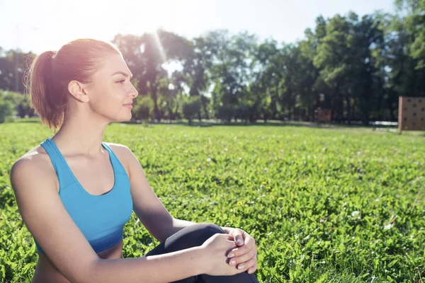 公園でリラックスしてスポーツウェアの美しい笑顔の女の子 トレーニングの後 緑の芝生の上に座って若い女性 晴れた夏の日に瞑想屋外 朝の演習と健康的なライフスタイル — ストック写真