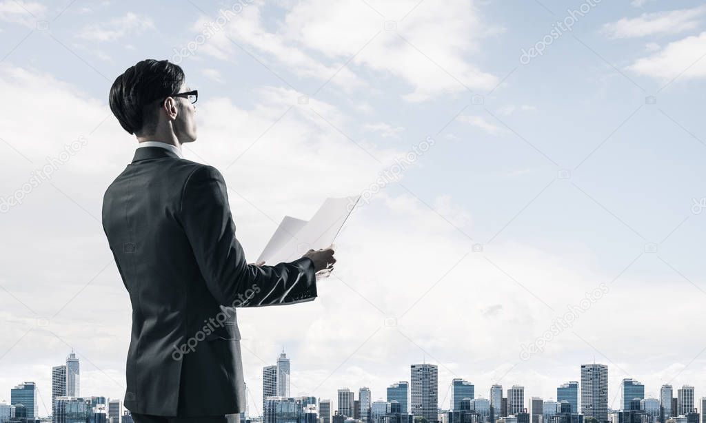 Young elegant businessman with papers in hands looking away