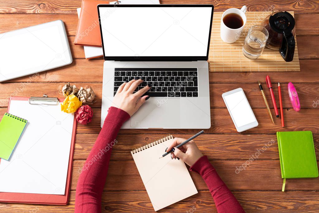 Business woman writing in notebook at office desk. Online business learning and education. Flat lay office workplace with female hands, laptop and documents. Digital technology and coworking space