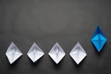 Siyah arka planda kağıt gemiler. Yaratıcı yenilik ve liderlik ticari konsepti. Mavi origami lideri diğer teknelerin önünde yatıyordu. Kopya alanı olan sosyal pazarlama düzeni.