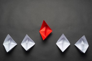 Siyah arka planda kağıt gemiler. Yaratıcı yenilik ve liderlik ticari konsepti. Beyaz teknelerin önünde düz kırmızı origami lideri yatıyordu. Şirket stratejisi ve başarılı çözüm.