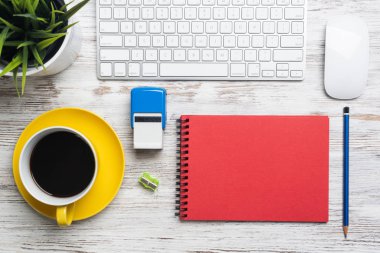 Modern ofis çalışanlarının çalışma alanı. İşte kahve zamanı. Düz tahta masa, bilgisayar klavyesi, lastik mühür, kırmızı defter ve saksıda yeşil bitki. İş ve ofis malzemeleri.
