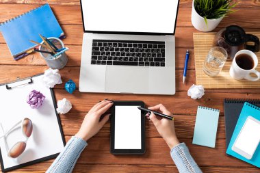 Ofis masasında çalışan bir iş kadını. Düz tahta masa, dizüstü bilgisayarı ve beyaz ekranlı tablet bilgisayarı vardı. Kadın eli ile üst düzey ofis işyeri. Çevrimiçi iş ve internet ticareti