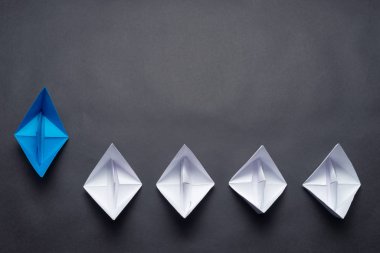 Siyah arka planda kağıt gemiler. Yaratıcı yenilik ve liderlik ticari konsepti. Mavi origami lideri diğer teknelerin önünde yatıyordu. Kopya alanı olan sosyal pazarlama düzeni.