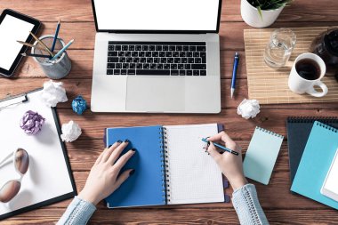 Ofis masasındaki not defterine yazan iş kadını. Çevrimiçi iş öğrenimi ve eğitim. Kadın eli, dizüstü bilgisayarı ve belgeleri olan düz ofis işyeri. Dijital teknoloji ve ortak çalışma alanı