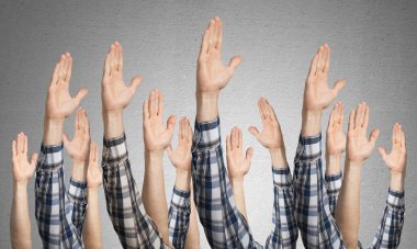 Oy verme jestini gösteren bir sıra adam eli. Katılım ve anlaşma işaretleri grubu. İnsan elleri gri duvarın arka planında siler. Birçok kol birlikte kaldırdı ve mevcut popüler jest.