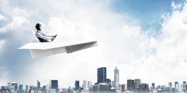 Kağıt uçakta oturan pilot ile iş motivasyonu kavramı. Havacı şapkalı komik adam ve şehrin üzerinde kağıt uçak süren gözlükler. Rüyada gökyüzünde uçmak. Yüksek binalarile modern megapolis.
