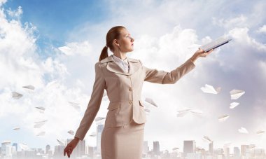 Çekici kadın mavi gökyüzünde cityscape ve kağıt uçaklar arka planda açık dizüstü tutan. Elinde açık kitap ile beyaz iş elbisesi zarif genç kadın. Şirkette staj ve uygulama.