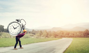 Miğferli adam arkada çalar saat taşıyor.