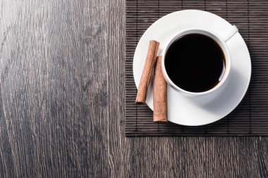 Masada bir fincan sade kahve. Üst görünüm beyaz fincan ve tarçın porselen tabak üzerinde sopalarla. Kafede taze ve aromatik sıcak içecekleri kapatın. Sabah kahvem. Bambu paspas ile Rustik ahşap masa.