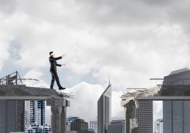 Gizli tehditlerin ve risklerin sembolü olarak beton köprüde gözü kapalı yürüyen bir iş adamı. Arka planda şehir manzarası. 3B görüntüleme.