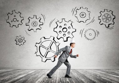 Beyaz kağıt kaplama giyen genç ve yakışıklı işadamı koşuyor ve duvarda dişli mekanizması var.