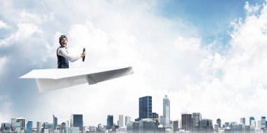Megapolis'in üstünde kağıt uçak kullanan havacı. Kağıt düzlemde oturan ve direksiyon u tutan pilotun yan görünümü. Yüksek gökdelenler ve ofis binaları ile Cityscape. Karma medya iş kavramı