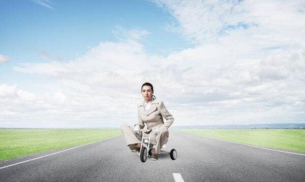 Beautiful caucasian woman riding kid's bicycle on asphalt road. Young employee in white business suit biking outdoor. Professional career start. Beginner level concept with female bicyclist.