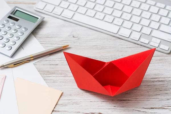 Businessman workspace at office desk with red paper ship. Flat lay table with calculator, business reports and pen. Close up red origami boat. Creative and innovative solution for business.