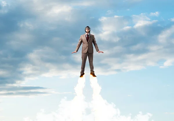 Businessman in suit and aviator hat flying in blue sky as superhero. Corporate manager as superman launching upwards with jet flame in stratosphere. Successful business startup motivation concept