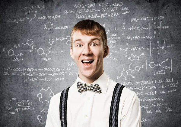幅広い笑顔で幸せな10代 感情的な赤毛の少年は数学的な計算をしている 若い科学者は 数式と黒板の背景に白いシャツ 蝶ネクタイ サスペンダーを身に着けています — ストック写真