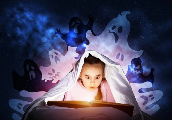 害怕的小女孩在床上读童话故事 书藏在毯子下的孩子 穿着睡衣的女孩和滑稽的鬼魂回到夜空 睡前和魔法故事阅读 从打开的书中闪耀着光芒 — 图库照片