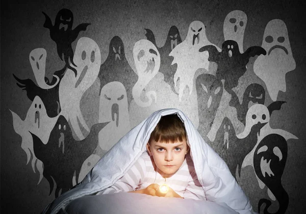 严肃的孩子 手电筒藏在毯子下 万圣节可怕的幽灵怪物在墙上 细心的孩子躺在家里的床上 害怕晚上在黑暗中睡觉 穿着睡衣的小男孩 — 图库照片