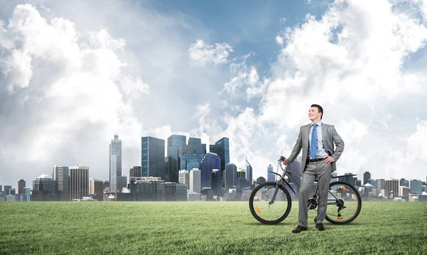 Good looking caucasian man in business suit posing on green meadow with bike. Happy businessman with bicycle relax on green grass at sunny day. Ecology transportation and environmental protection
