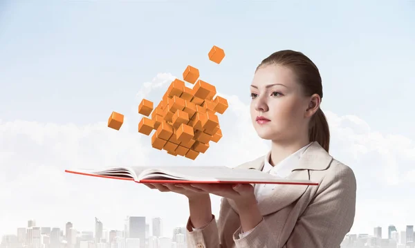 Young woman holding open notebook with flying abstract 3d cubes. Hi-tech concept with virtual reality element. Closeup open book in female hands. Elegant lady on background of modern cityscape and sky