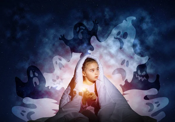 Scared girl with flashlight hiding under blanket from imaginary phantoms. Frightened kid sitting in bed on night sky background. Night terrors of child. Girl in pajamas and boo ghosts silhouettes